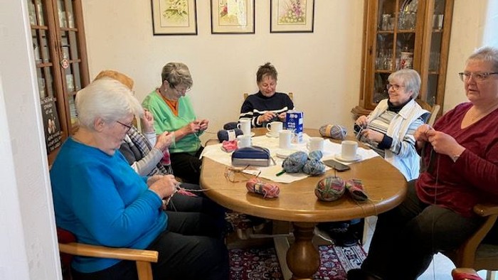 Eine Gruppe älterer Frauen versammelte sich um einen Tisch und war mit Stricken und Handarbeiten beschäftigt.