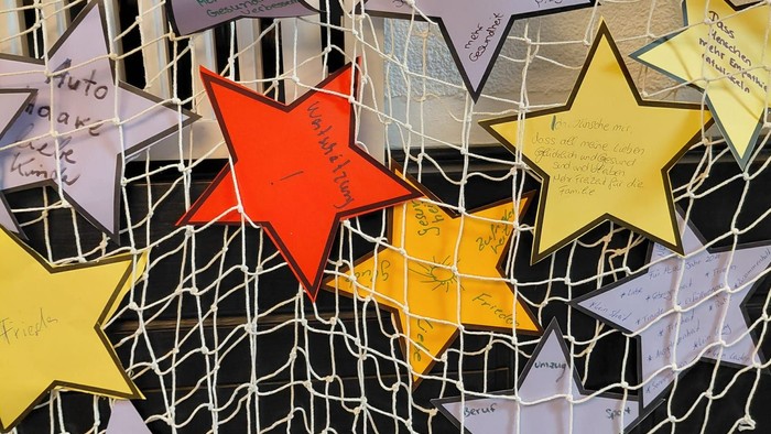 Bunte sternförmige Zettel mit handschriftlichen Nachrichten, die an einem Fischernetz hängen.