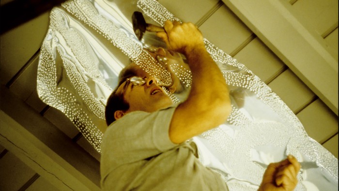 En person, der ligger i sengen og holder en mobiltelefon og et hvidt mønstret pudebetræk.