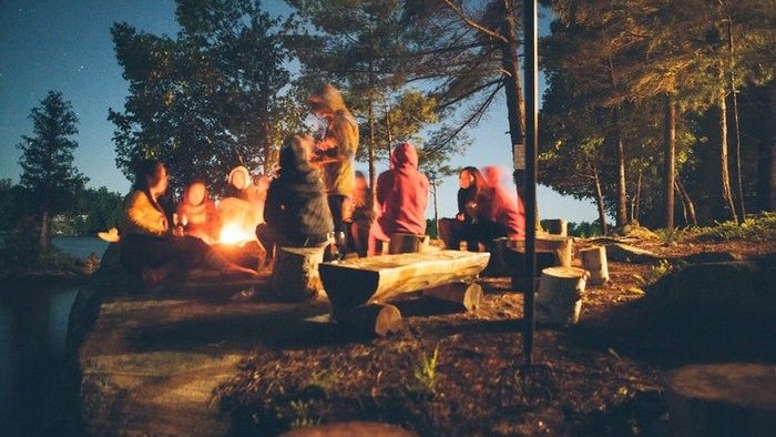 Eine Gruppe von Menschen sitzt um ein Lagerfeuer im Wald.