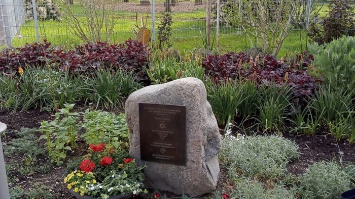 Ein gestaltetes Gartengrundstück mit einem Gedenkstein, umgeben von farbenfrohen Blumen und Grünpflanzen.