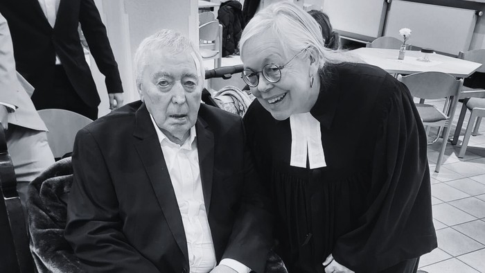 Zwei Personen, eine im Rollstuhl und eine daneben stehend, wirken fröhlich in ein Gespräch vertieft – drinnen.