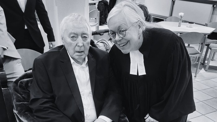 Zwei Personen, eine im Rollstuhl und eine daneben stehend, wirken fröhlich in ein Gespräch vertieft – drinnen.