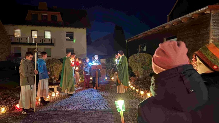 Eine nächtliche Zusammenkunft mit kerzenbeleuchteten Figuren in historischen Kostümen, die im Freien nahe beleuchteter Häuser auftreten.