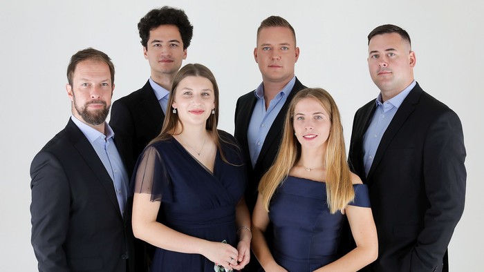 Formelles Gruppenporträt von fünf Erwachsenen und zwei jungen Frauen in professioneller Kleidung, die gemeinsam posieren.