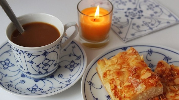 Eine Tasse Kaffee, ein Stück Kuchen und eine brennende Kerze.