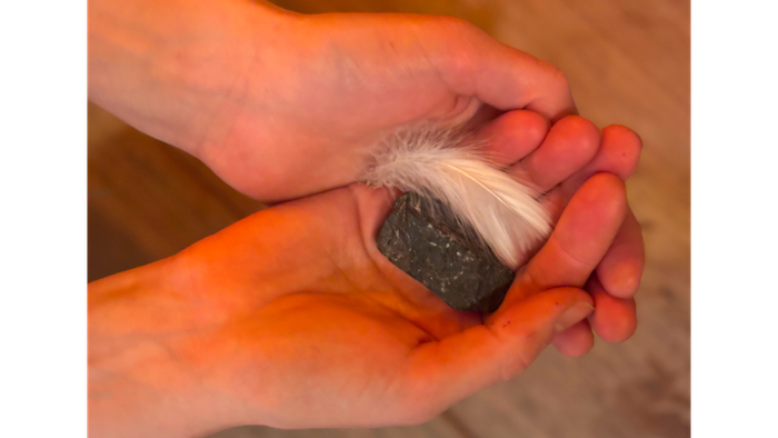 Eine Frau hält zwei H#nde übereinander und darin einen Stein und eine Feder.