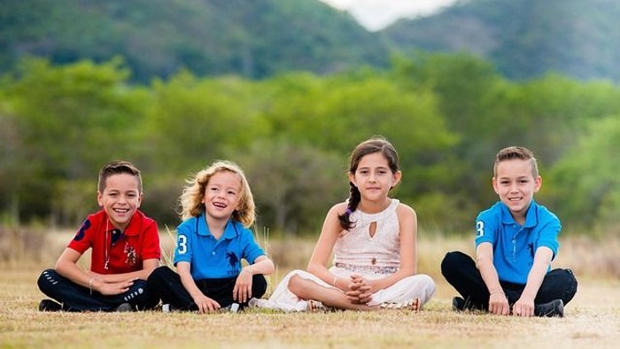Vier fröhliche Kinder, die glücklich zusammen auf einer üppigen, grünen Wiese im Freien sitzen.