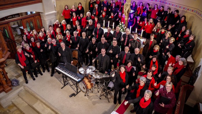 Große Chorgruppe posiert gemeinsam mit Musikinstrumenten auf der Bühne.