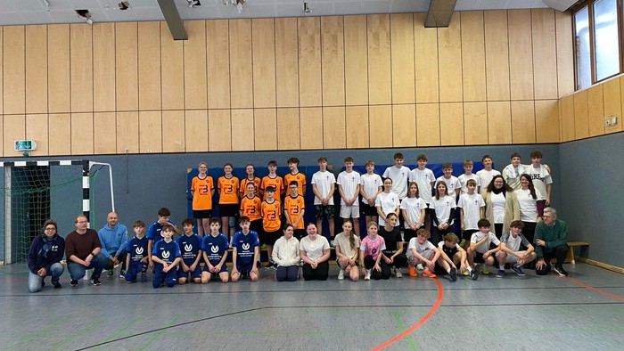 Gruppe von Kindern und Erwachsenen, die in einer Turnhalle für ein Teamfoto posieren.