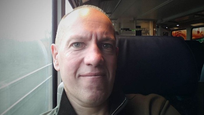 En bald, smilende mand sitter i en bus.