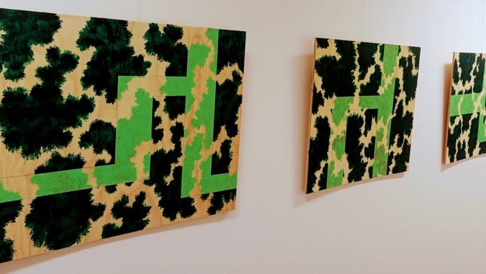 Abstrakt kunst med markante grønne former på sort-og-grønne mønstrede lærreder, arrangeret på en væg.