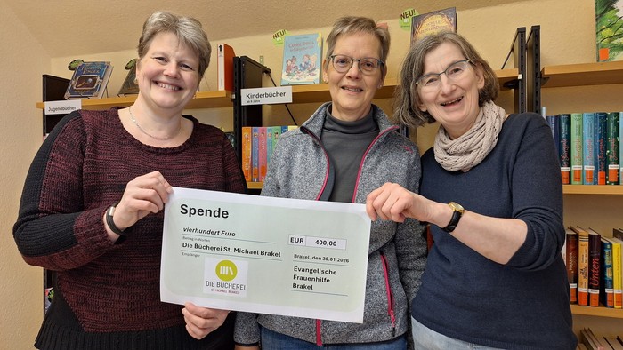 Elisabeth Dohmeier (mi.) und Sonja Walle (re.) von der Evangelischen Frauenhilfe überreichen in den Räumen der Bücherei einen symbolischen Spendenscheck an Andrea Held (li.) vom Leitungsteam