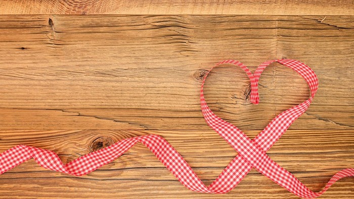 Ein rot kariertes Band in Herzform, das auf einer Holzoberfläche liegt.