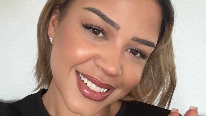 En glad person, der smiler bredt i en sort top og vinker med en ring på hånden.