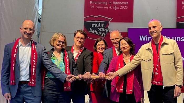 Eine Gruppe von Menschen feiert bei einem Event in Hannover, alle tragen rote Schals und lächeln.