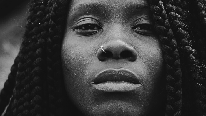 Im Mittelpunkt eine Frau mit dunkler Haut, einem Nasenring und vielen geflochtenen Zöpfen