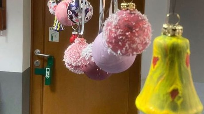 Bunte handgefertigte Weihnachtsbaumschmuckstücke, darunter Pompons und eine glockenförmige Dekoration, die an einer Tür hängen.