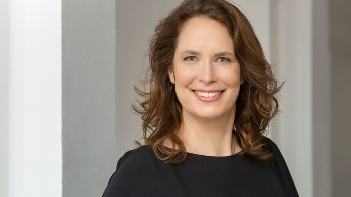 Professionelle Frau in einem schwarzen Kleid, die selbstbewusst in einem Flur steht und ein warmes Lächeln zeigt.