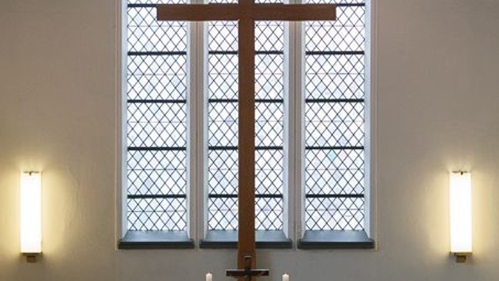 Elegante Kircheninnenausstattung mit einem hohen Kruzifix, bunten Glasfenstern und einem geschmückten Altar mit Kerzen und Blumen.