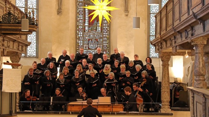 Ein großer Chor tritt in einer prächtigen Kirche mit klassischen Buntglasfenstern und aufwendiger Architektur auf.