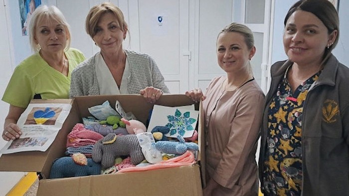 Vier Frauen posieren stolz mit einer Kiste voller gespendeter Kleidung und Babyartikel.