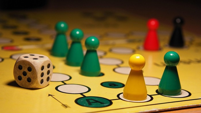 Eine Nahaufnahme eines Brettspielaufbaus mit bunten Spielfiguren und einem Würfel auf einem gelben Spielbrett.