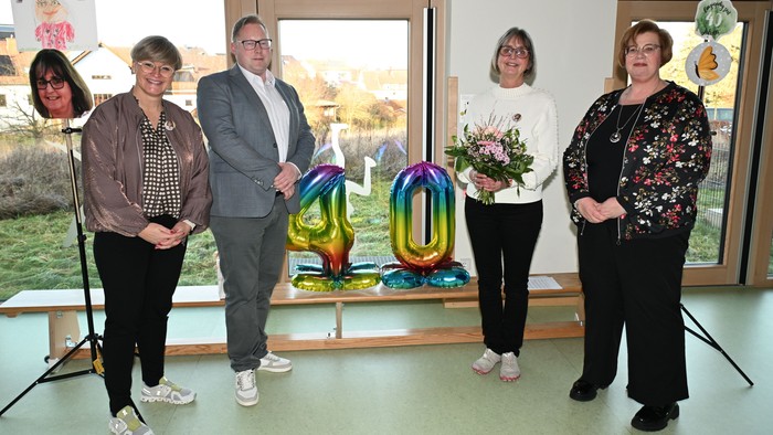 Gruppe von Menschen, die drinnen in der Nähe von bunten Ballonskulpturen und einem Blumenstrauß posieren.