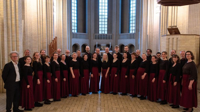 En stor korgruppe i formelt tøj, der optræder i en stor katedral med høje, buede vinduer.