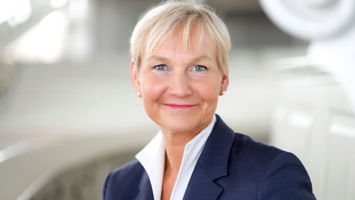 Eine professionelle Frau mit kurzem Haar in einem blauen Blazer lächelt.