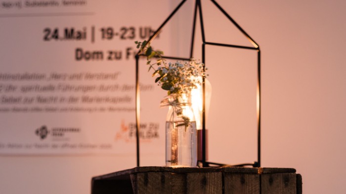 Herzlich willkommen-Schild mit LED-Lichtern, das „Herzlich Willkommen“ neben einer Lebensmittelauslage und einer dekorativen Laterne anzeigt.