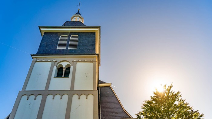 Ein hoher Kirchturm mit einer dunklen Spitze und Bogenfenstern unter einem klaren blauen Himmel.