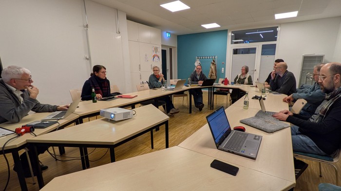Eine Gruppe von Personen sitzt um einen großen Tisch mit Laptops und Papieren und ist in ein Meeting vertieft.
