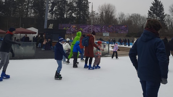 Menschen, die an einem bewölkten Tag im Freien Schlittschuh laufen, mit Zuschauern und einem festlichen Hintergrund.