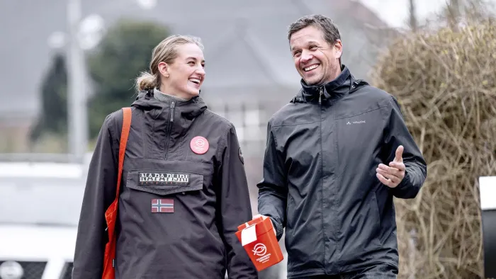 To personer smiler og går udendørs iført sportstøj og holder en rød genstand.