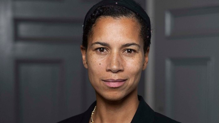 Professionel kvinde i en mørk blazer, der poserer selvsikkert med elegant smykker.