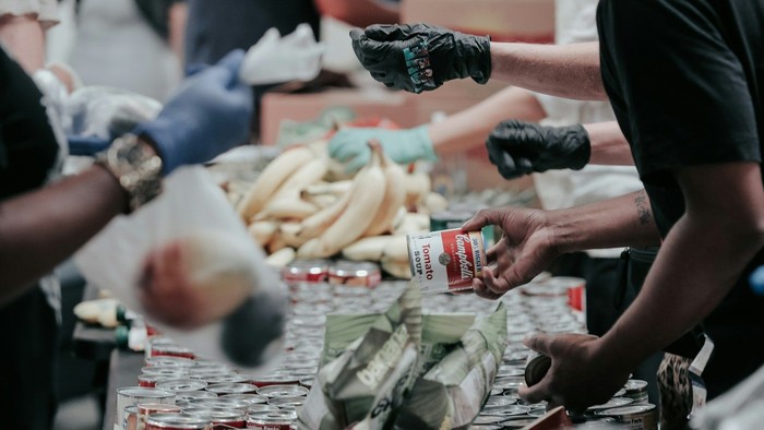 Mehrere Menschen verteilen gespendete Lebensmittel, hauptsächlich in Dosen