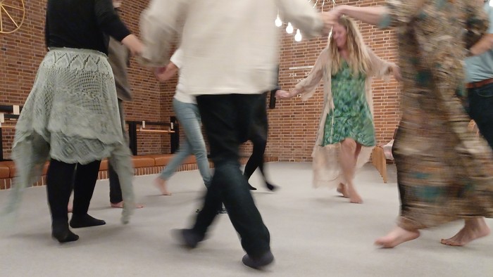 Gruppe af mennesker, der danser energisk i et rummeligt indendørs område med sløret bevægelse.