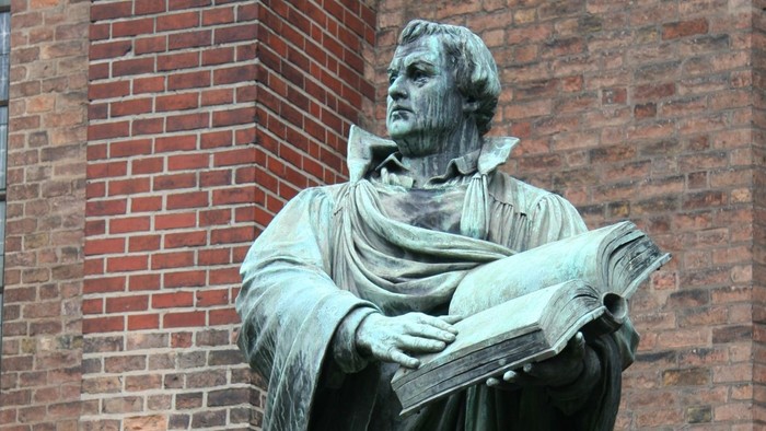 Statue eines Mannes mit Buch vor Ziegelmauer