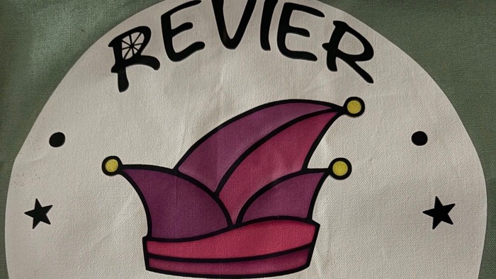 Ein runder Aufnäher mit einem rosa Clownshut mit Sternen und dem Text „Revier Schicksen“ mit einem Herz.