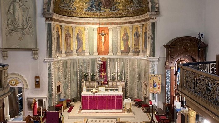 Elegante Kircheninnenausstattung mit prunkvollem Altar, Buntglasfenstern und hölzernen Kirchenbänken mit reichen Verzierungen.