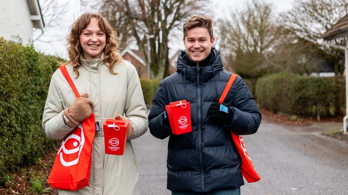 To glade mennesker holder røde kaffekopper og poser på en villavej.