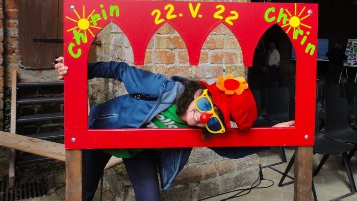 Eine Person posiert mit einem roten Schild, das vorgibt, ein Clown zu sein, der bei einem Date hinfällt, markiert mit „22.V.22“.