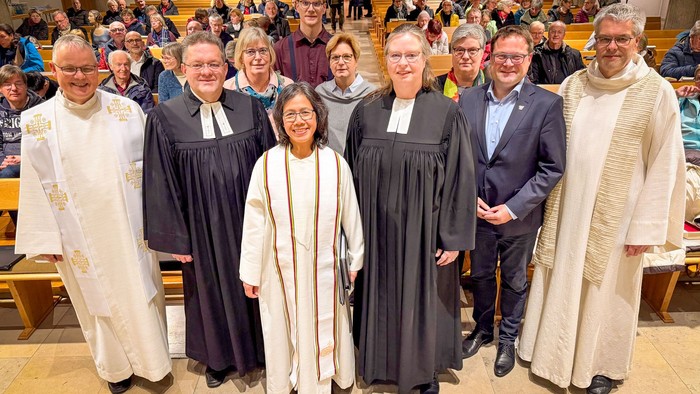 Mehrere Pfarrpersonen im Talar oder Albe mit weiteren Personen vor einem gut besetzten Kirchraum