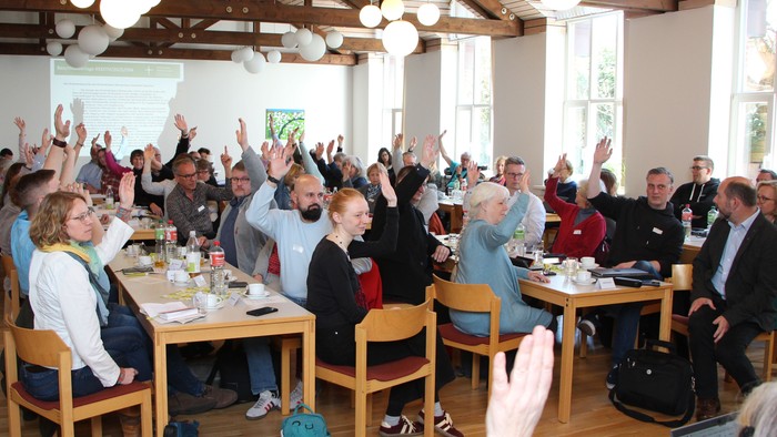 Ein großer Raum mit vielen Menschen an Tischen, die aufstehen und klatschen.