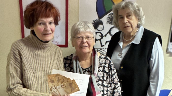 Drei Frauen posieren gemeinsam mit einem gerahmten Kunstwerk und einer Urkunde in einem Innenraum.