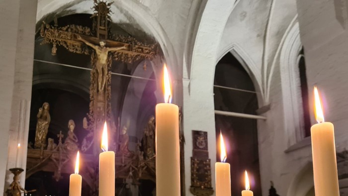 Lebendige Kerzen erhellen ein feierliches Kruzifix in einem prunkvollen, gewölbten Kircheninneren.