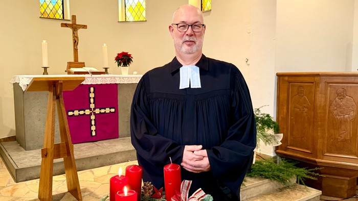Mann in religiöser Kleidung steht in der Nähe von Weihnachtsdekorationen und einem Altar.