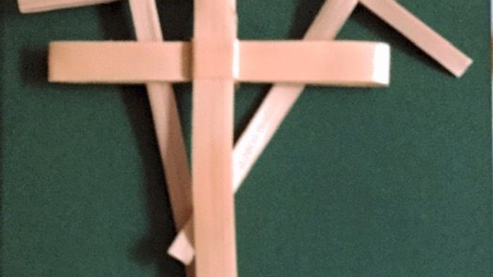 Three wooden sticks arranged to form a stylized, overlapping cross pattern against a green background.