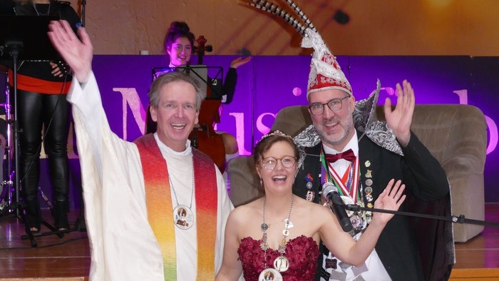 Festliche Veranstaltung mit gekröntem König, Königin und Prinz mit Regenbogen-Schärpe und zeremoniellen Kronen.